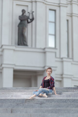 Girl ballerina in jeans, a plaid shirt and pointe shoes dancing in the city on the street © Tatiana