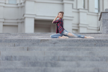 Girl ballerina in jeans, a plaid shirt and pointe shoes dancing in the city on the street © Tatiana