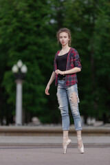 Girl ballerina in jeans, a plaid shirt and pointe shoes dancing in the city on the street © Tatiana