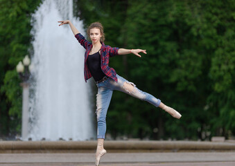 Girl ballerina in jeans, a plaid shirt and pointe shoes dancing in the city on the street © Tatiana