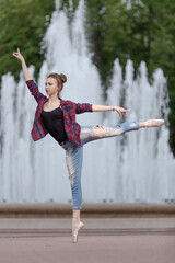 Girl ballerina in jeans, a plaid shirt and pointe shoes dancing in the city on the street © Tatiana
