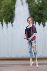 Girl ballerina in jeans, a plaid shirt and pointe shoes dancing in the city on the street © Tatiana
