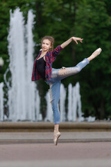 Girl ballerina in jeans, a plaid shirt and pointe shoes dancing in the city on the street © Tatiana