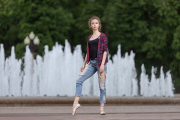 Girl ballerina in jeans, a plaid shirt and pointe shoes dancing in the city on the street © Tatiana