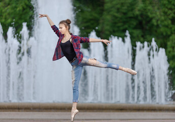 Girl ballerina in jeans, a plaid shirt and pointe shoes dancing in the city on the street © Tatiana