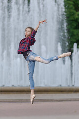 Girl ballerina in jeans, a plaid shirt and pointe shoes dancing in the city on the street © Tatiana
