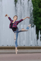Girl ballerina in jeans, a plaid shirt and pointe shoes dancing in the city on the street © Tatiana
