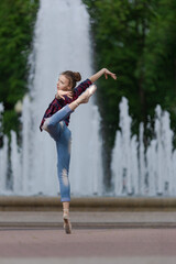 Girl ballerina in jeans, a plaid shirt and pointe shoes dancing in the city on the street © Tatiana