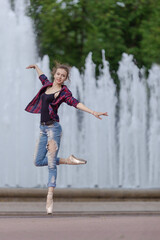 Girl ballerina in jeans, a plaid shirt and pointe shoes dancing in the city on the street © Tatiana
