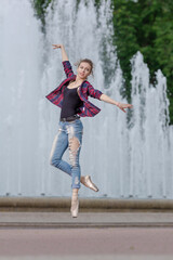 Girl ballerina in jeans, a plaid shirt and pointe shoes dancing in the city on the street © Tatiana