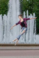 Girl ballerina in jeans, a plaid shirt and pointe shoes dancing in the city on the street © Tatiana