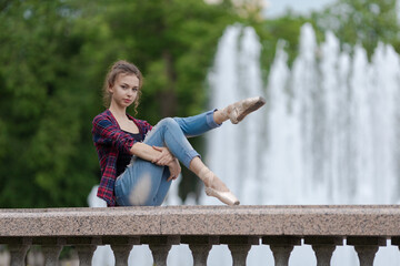 Girl ballerina in jeans, a plaid shirt and pointe shoes dancing in the city on the street © Tatiana