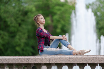 Girl ballerina in jeans, a plaid shirt and pointe shoes dancing in the city on the street © Tatiana