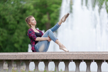 Girl ballerina in jeans, a plaid shirt and pointe shoes dancing in the city on the street © Tatiana
