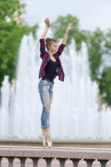 Girl ballerina in jeans, a plaid shirt and pointe shoes dancing in the city on the street © Tatiana