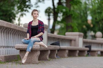 Girl ballerina in jeans, a plaid shirt and pointe shoes dancing in the city on the street © Tatiana