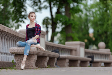 Girl ballerina in jeans, a plaid shirt and pointe shoes dancing in the city on the street © Tatiana