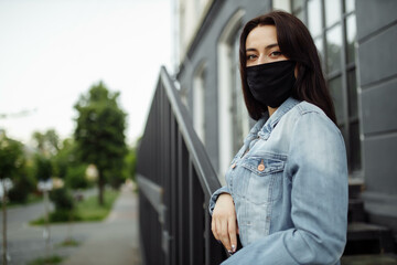 girl in a protective mask on a balcony looks at an empty city