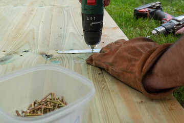 A man drilling holes to fix metal hinges to a wooden door.  DIY concept with a box of screws in the...