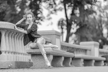 Fototapeta na wymiar Black and white photo of a ballerina girl in jeans and pointe shoes, dancing and posing in the city on the street