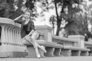 Black and white photo of a ballerina girl in jeans and pointe shoes, dancing and posing in the city on the street © Tatiana