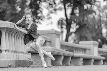 Black and white photo of a ballerina girl in jeans and pointe shoes, dancing and posing in the city on the street © Tatiana
