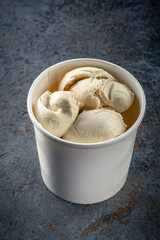 Three balls of vanilla-nut ice cream in a white paper Cup on a gray stone background