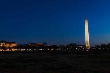 Tall high Washington Monument memorial in blue sky at evening night in winter, lawn, illuminated bright lights dark in December