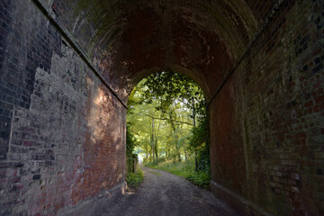 Red brick tunnel contains a muddy double-track lane that opens out into deciduous forest greenery.