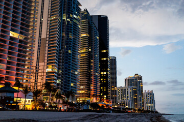 Sunny Isles Beach, apartment condo hotel buildings during dark night illuminated colorful colors in Miami, Florida with skyscrapers sand, coastline, lifeguard tower
