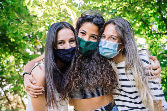 Portrait of group young millennials friends embraced in a park at sunset in summer - Women looking the camera and smiling below face mask avoid infection from virus of Coronavirus, Covid-19
