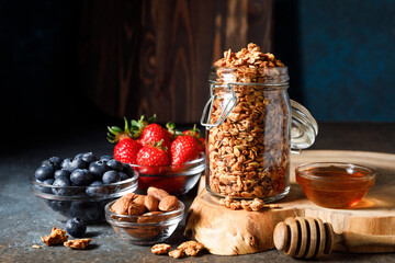 Homemade oatmeal granola in glass jar with berries on dark background.