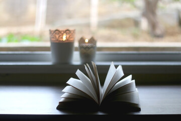 Open book and candle holders with lit candles at home. Selective focus.