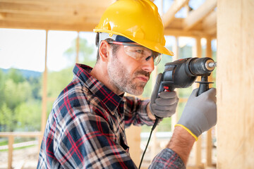 Worker using drill working on construction of wood frame house