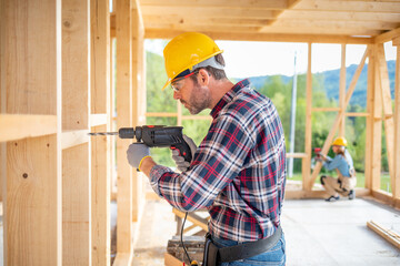 Worker using drill working on construction of wood frame house