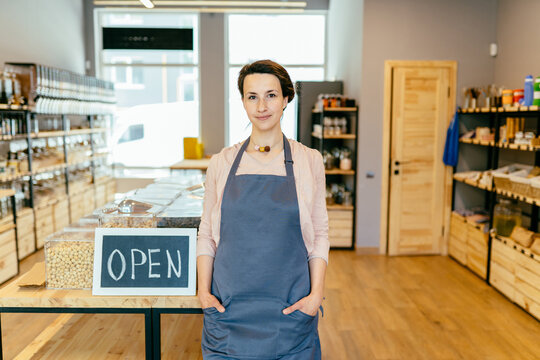 Reopening Of A Small Business Activity After The Covid-19 Emergency, Ended The Lockdown And Quarantine. Business Woman Owner Holding Sign That Says Now We Are Open Support Local Businesses.