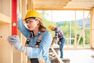 Woman worker at building site of wood frame house using level tools
