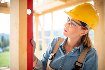 Woman worker at building site of wood frame house using level tools