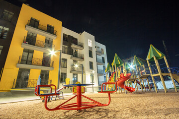 Fototapeta na wymiar Children playground at night in residential district yard between apartment buildings.