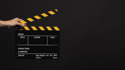 Fototapeta na wymiar A hand is holding black with yellow color clapper board or movie slate use in video production and film industry on black background.