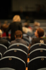 Blur defocus texture, background for design. Spectators in the theater sit on chairs before the...