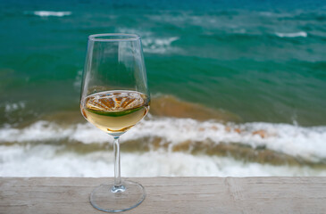 A glass of white wine against the blue sea, close-up