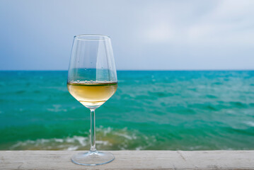 A glass of white wine against the blue sea, close-up