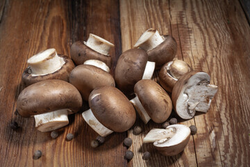 Royal mushrooms champignon whole and cut into pieces, scattered peppers, close-up on a wooden background, rustic style