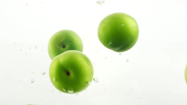 Plums spinning, floating and splashing into water on white background. Fresh organic fruit falling in slow motion 4K cinematic closeup background video with real shot 120 fps bubbles and particles.