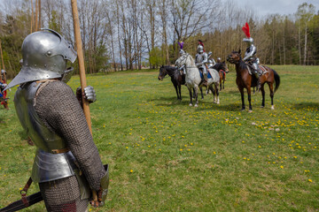 A knight in vintage armor of the 15th century rides a horse across a field for a tournament