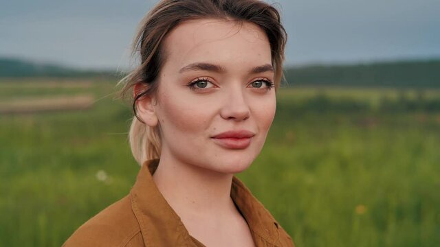 Woman with plump lips and Attractive Appearance looking at Camera. Smiling girl with natural Beauty standing at Countryside, having simple hairstyle. Empty and large Fields in the Background.