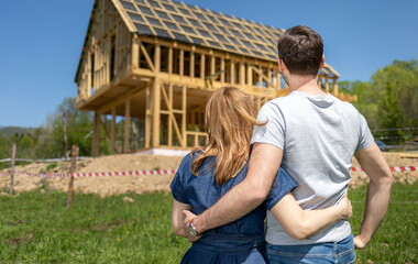 Happy couple outdoor looking at their new home house under construction
