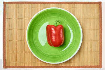 red pod of sweet bell pepper on a green plate on a cane place mat