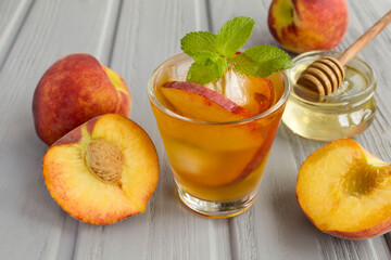 Cold tea with peaches in the glass on the grey wooden background
